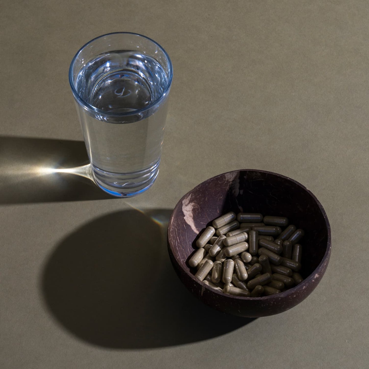 Bowl of Royal Kratom Maeng Da Grand Kratom Capsules in a bowl near a glass of water