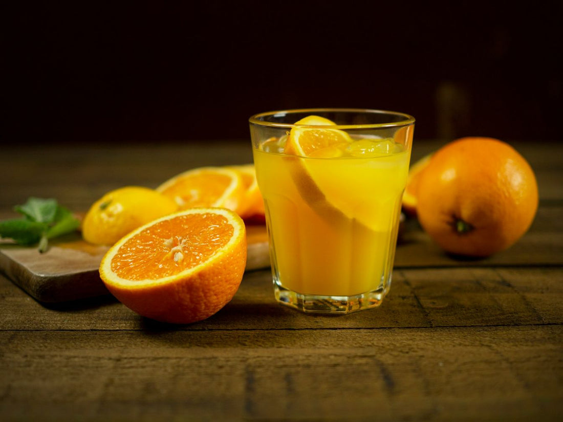 A glass of orange juice next to sliced oranges