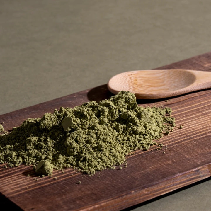 Green kratom powder piled onto a wooden board beside a wooden poon