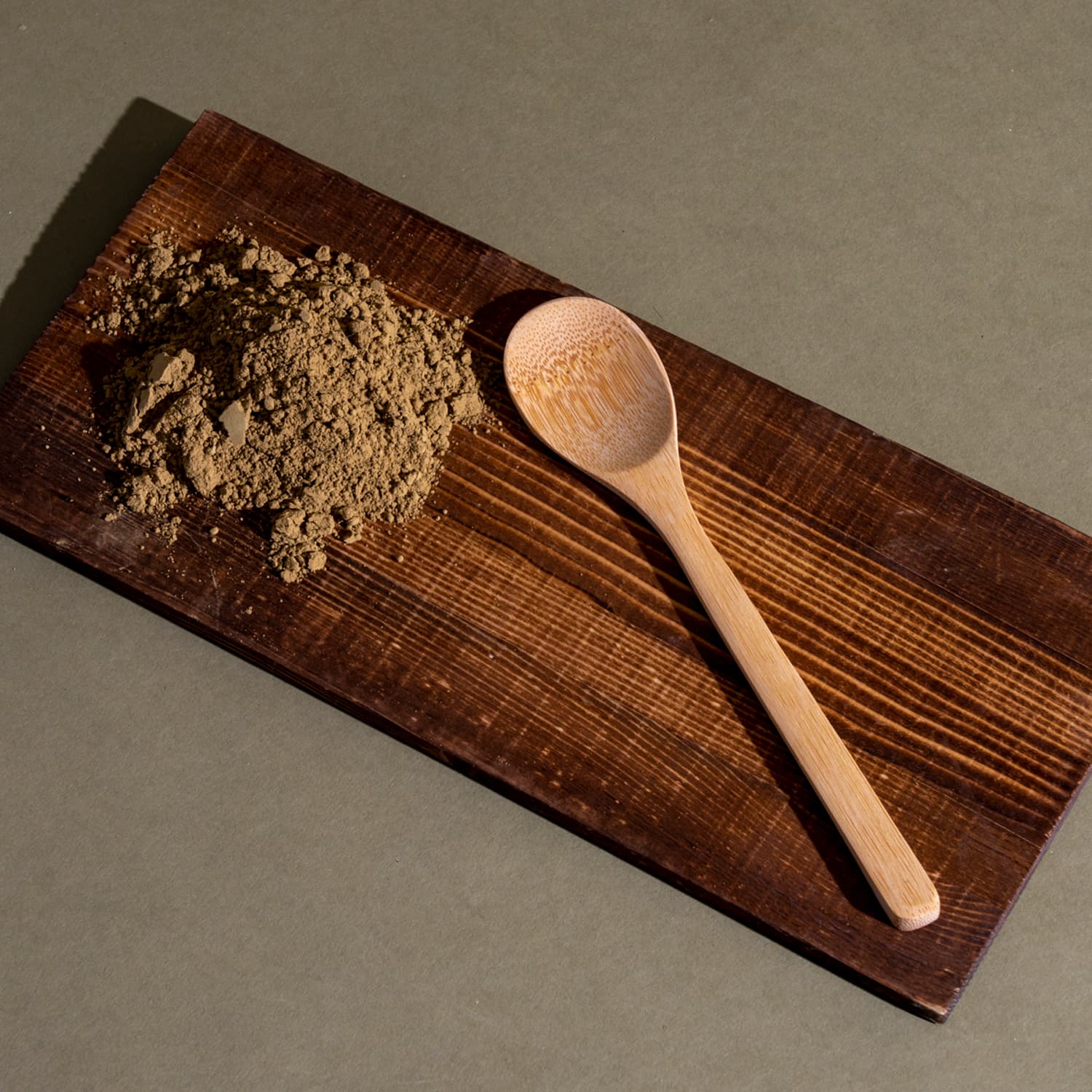 A wooden cutting board with a spoon and brown powder