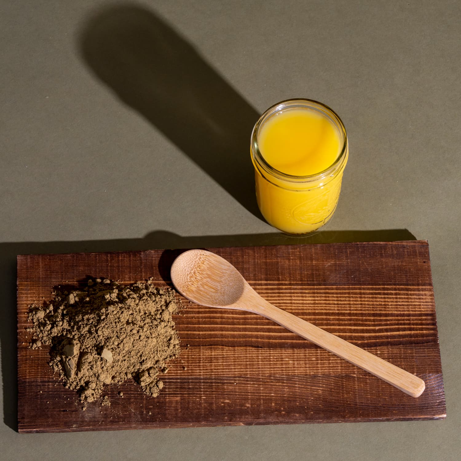 A wooden cutting board with a spoon and brown powder next to a glass of orange juice
