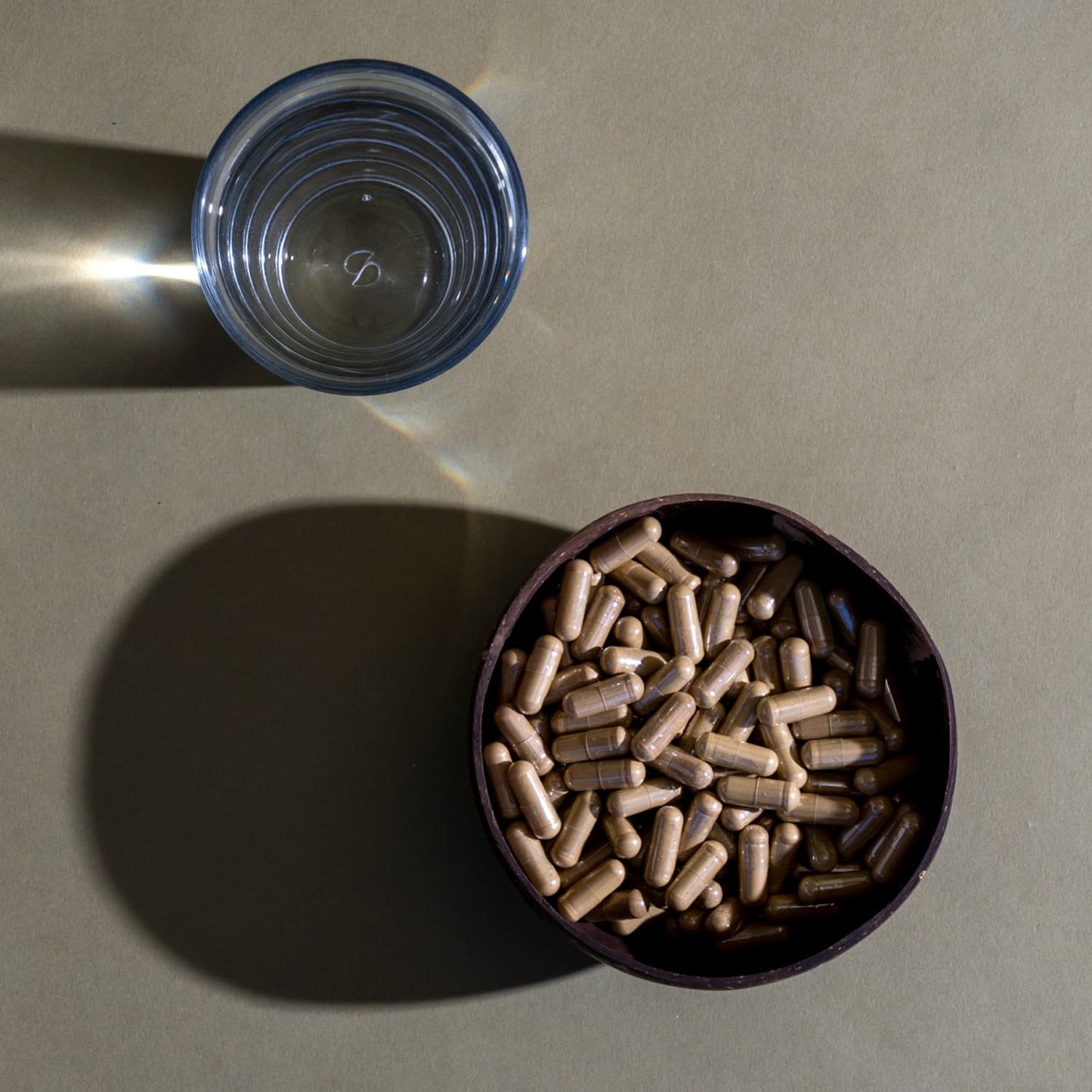 A bowl of brown capsules and a glass of water on a table