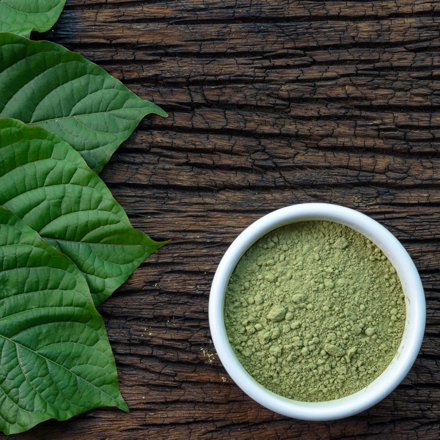 Green vein kratom powder in a bowl on a wooden table