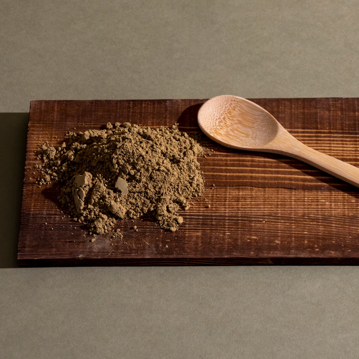 A spoon and brown powder on a wooden cutting board