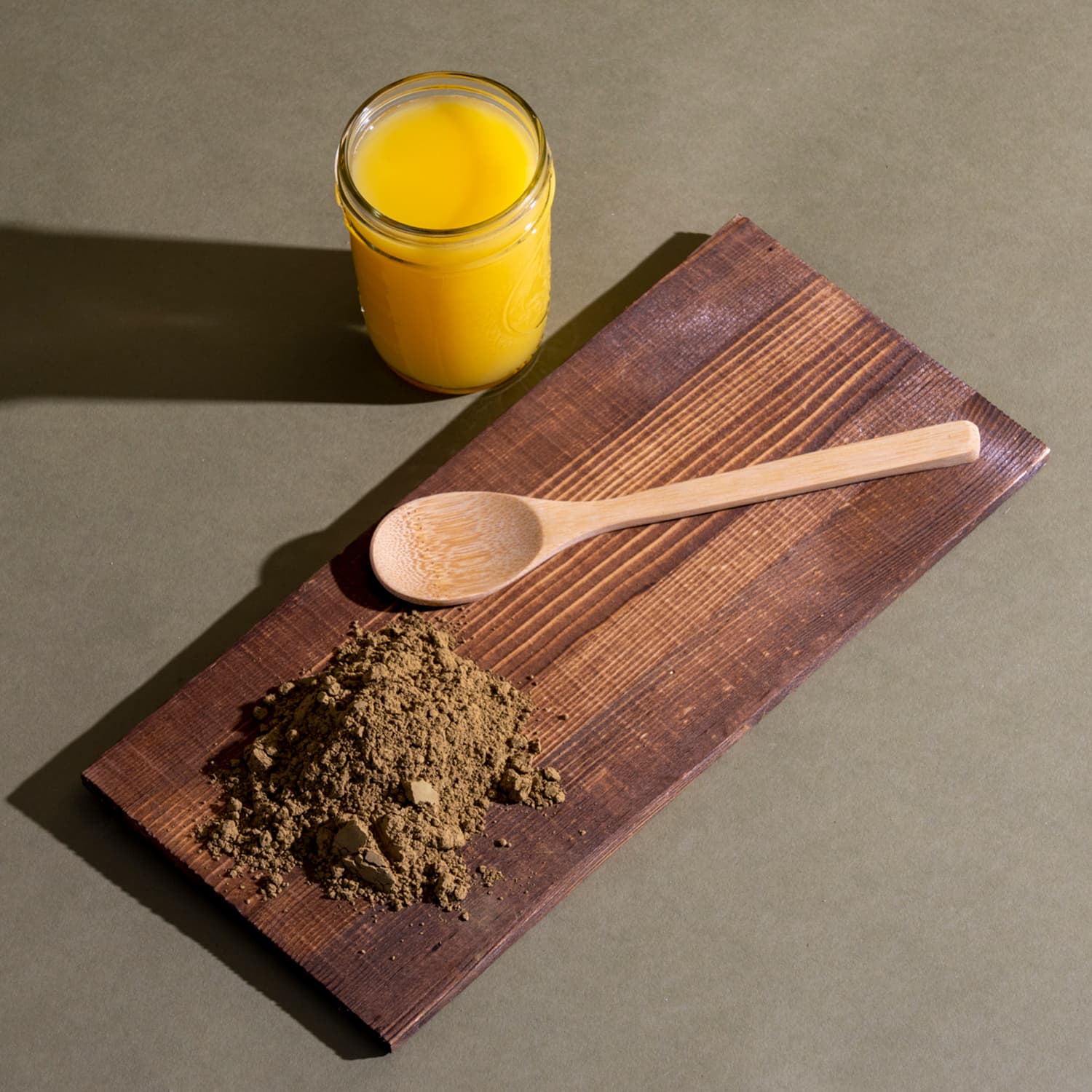 Wooden cutting board with a spoon and brown powder next to a glass of orange juice