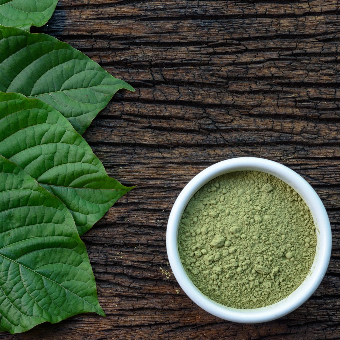 Green vein kratom powder in a bowl on a wooden table