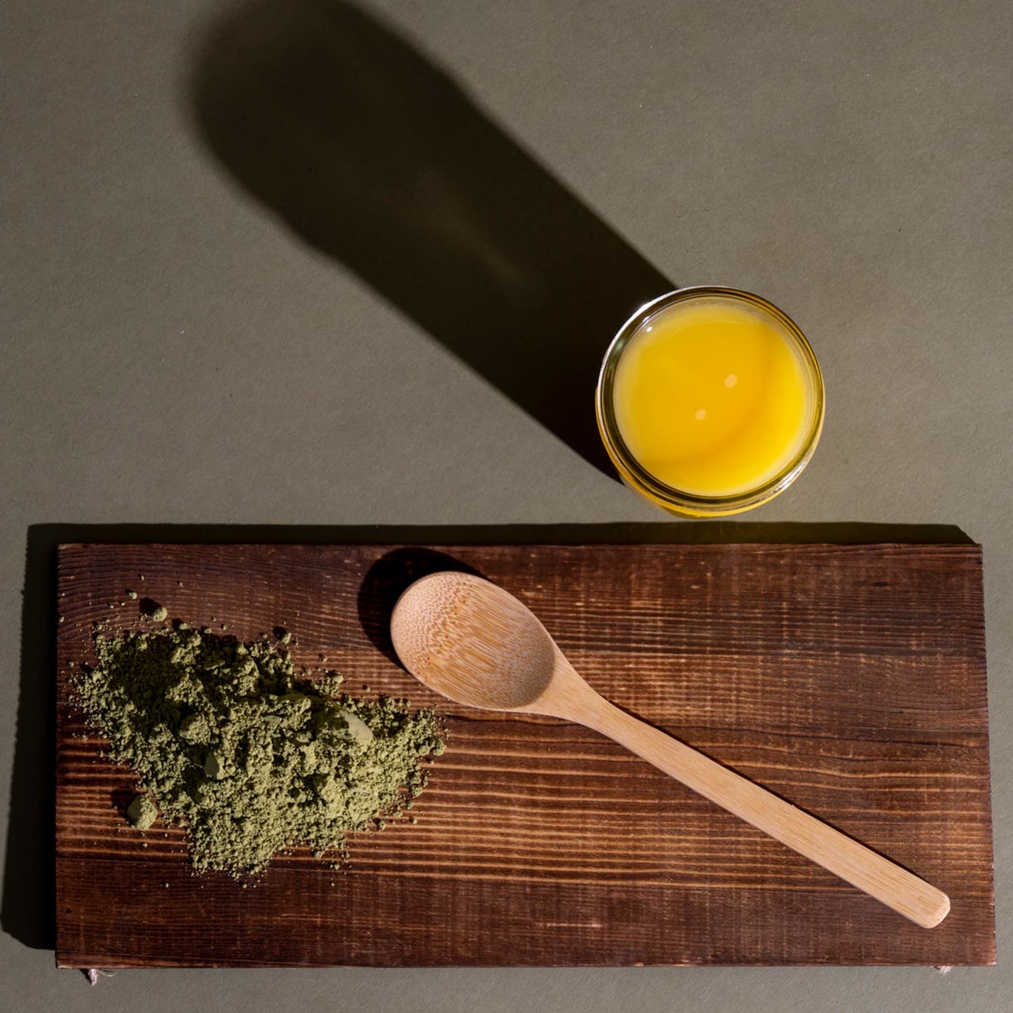 A wooden cutting board with a spoon and brown powder next to a glass of orange juice