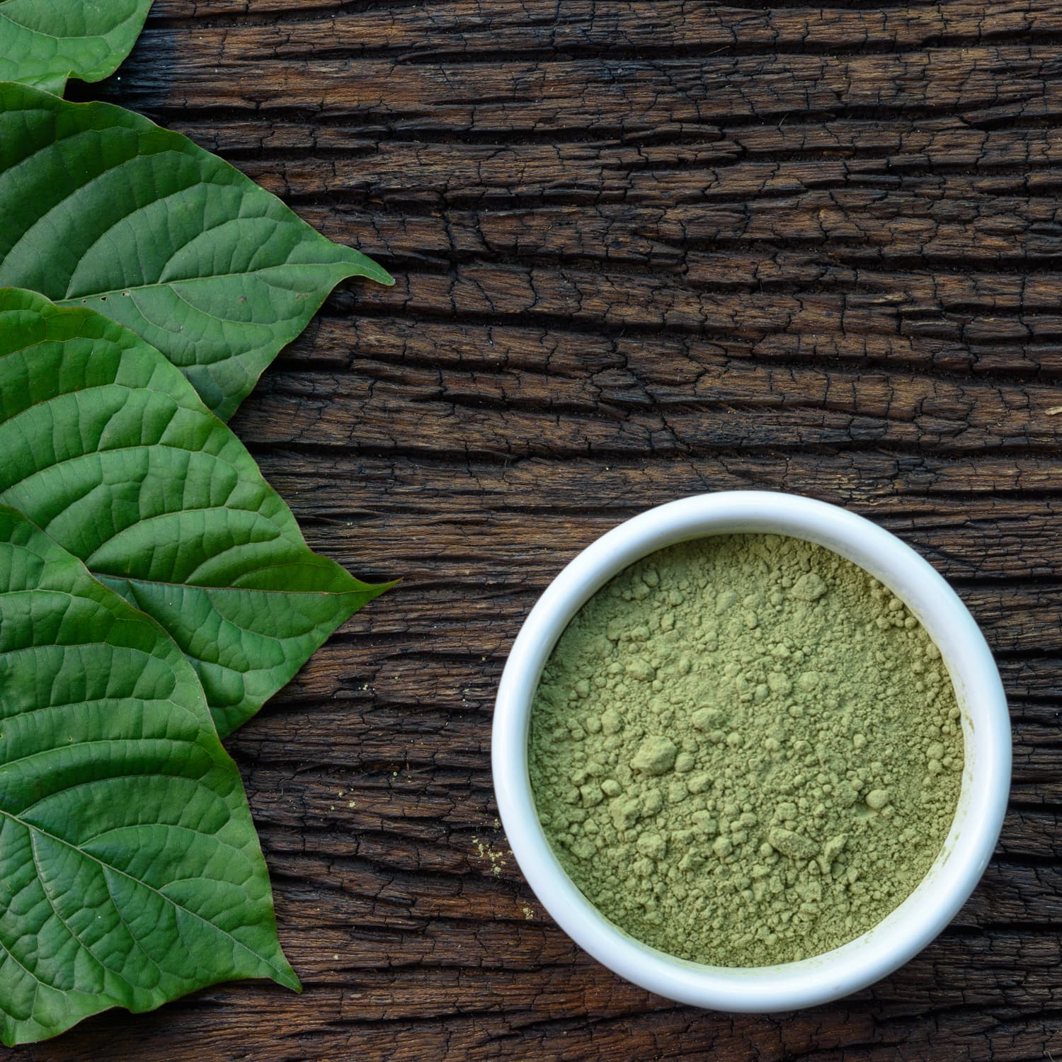 Green vein kratom powder in a bowl on a wooden table