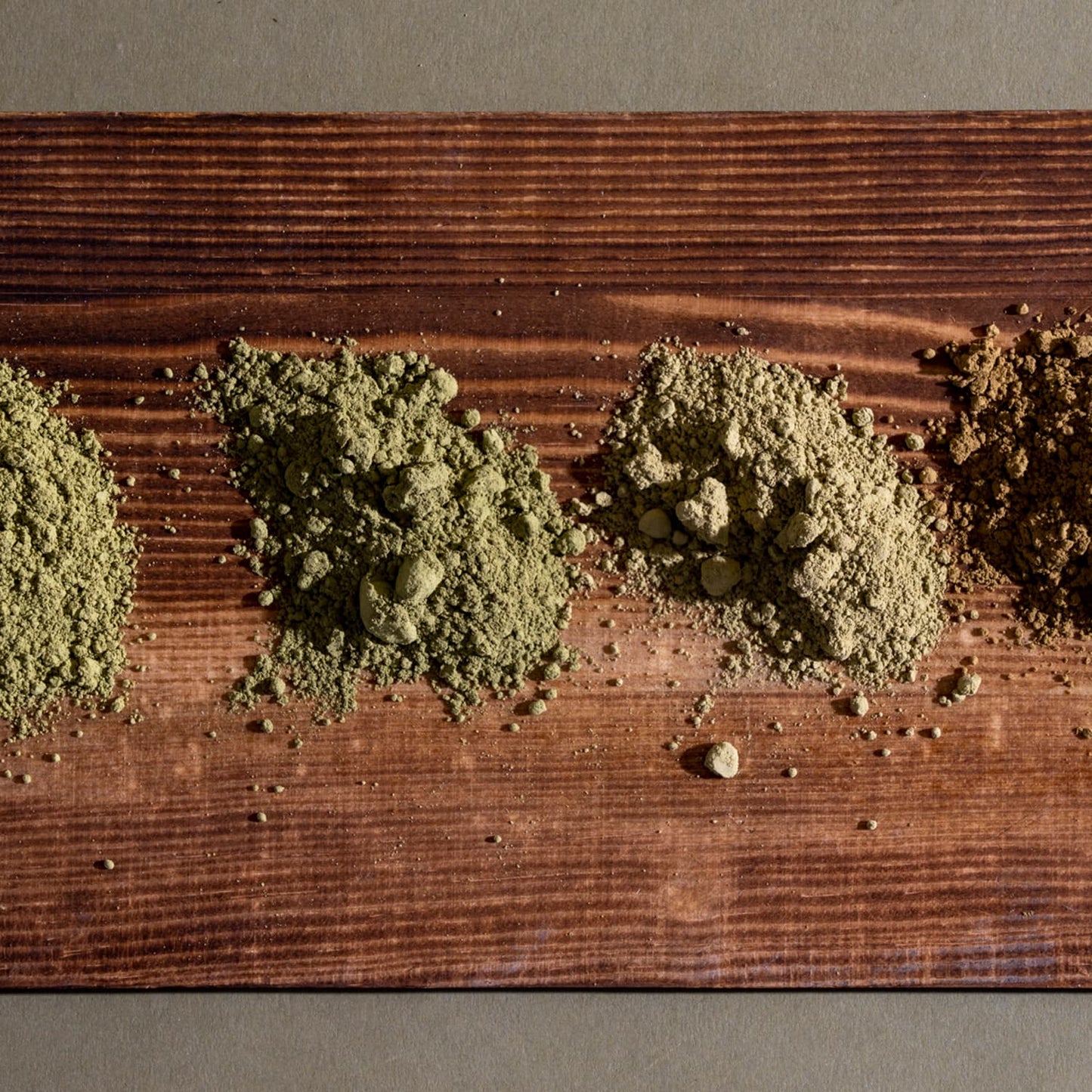A close-up image of four kratom powder piles on a wooden board