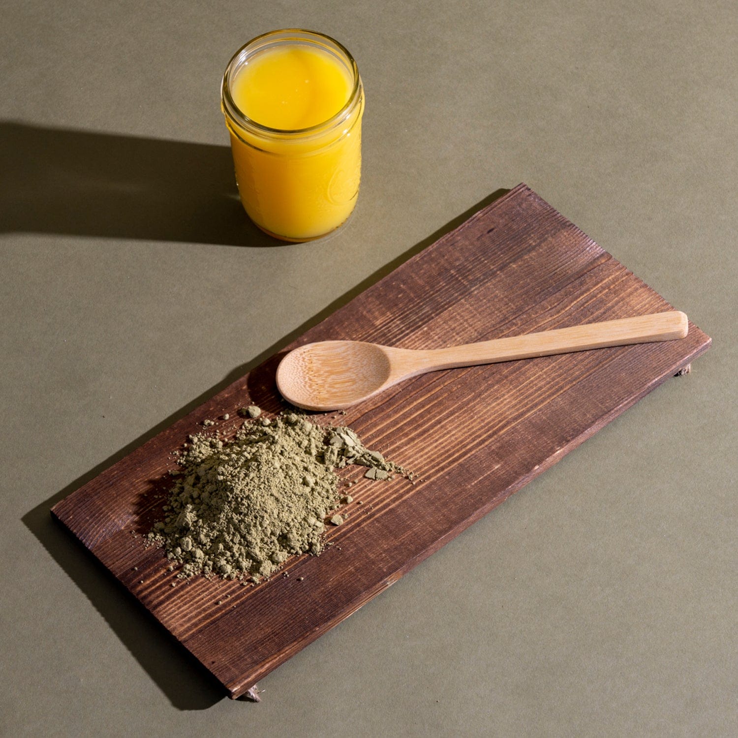 A spoon and kratom powder on a wooden board beside a glass of orange juice